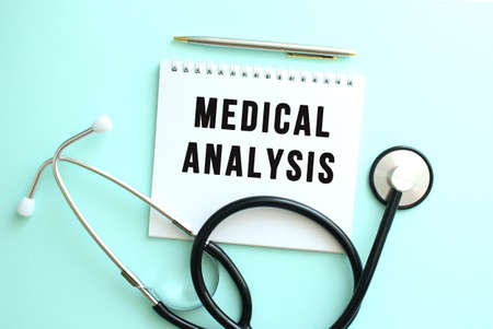 White notepad with the words MEDICAL ANALYSIS and a stethoscope on a blue background.の写真素材