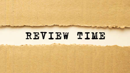 Text REVIEW TIME appearing behind torn brown paper. Top view.の写真素材