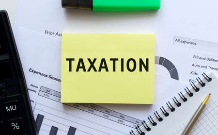 Text TAXATION on the page of a notepad lying on financial charts on the office desk. Near the calculator. Business concept.の写真素材