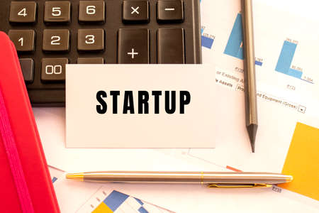 Text STARTUP on white card with metal pen, calculator and financial charts. Business and financial conceptの写真素材