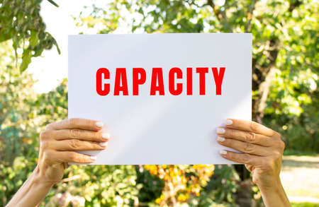 Female hands hold a sheet of white paper with the text CAPACITY on the background of nature. information poster.の写真素材
