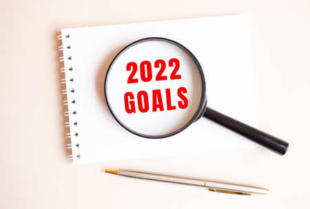 The magnifying glass rests on the pad and shows 2022 GOALS on a white page. There is a pen next to it.の写真素材