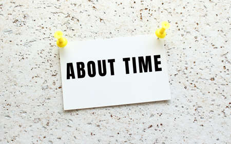 ABOUT TIME is written on a card attached to a white textured wall with a button. Office reminder.の写真素材