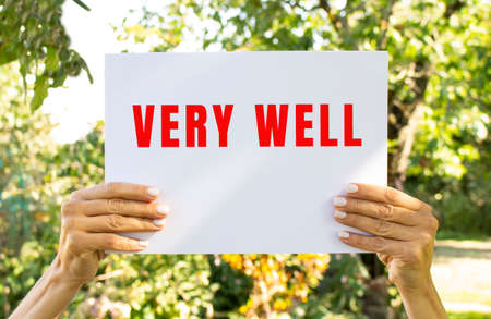 Female hands hold a sheet of white paper with the text VERY WELL on the background of nature.の写真素材