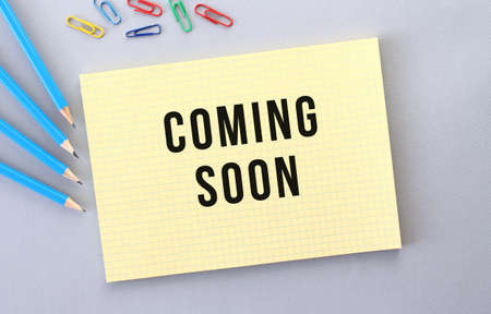 COMING SOON text in notebook on gray background next to pencils and paper clips.の写真素材