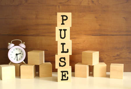 Five wooden cubes stacked vertically to form the word PULSE on a brown background.の写真素材