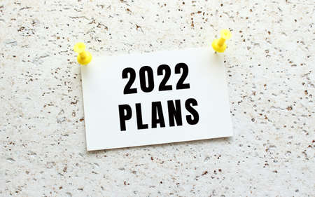 2022 PLANS is written on a card attached to a white textured wall with a button. Office reminder.の写真素材
