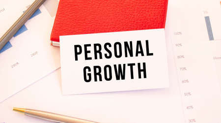 White business card with text PERSONAL GROWTH lies next to red business card holder.の写真素材