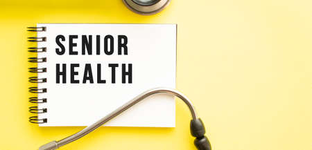 Text SENIOR HEALTH on notebook with stethoscope on yellow background. medical concept.の写真素材