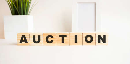 Wooden cubes with letters on a white table. The word is AUCTION. White background with photo frame, house plant.の写真素材