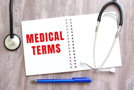 White notebook with red text MEDICAL TERMS and a stethoscope on a gray wooden table. medical conceptの写真素材