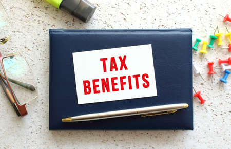 Text TAX BENEFITS on a business card lying on a blue notebook next to the glasses and stationery. business concept.の写真素材
