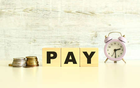 There are three wooden cubes with letters on the table next to the coins. The word PAY. On a gray background. Front View Conceptsの写真素材