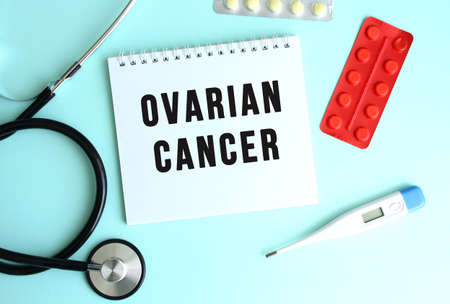 The text OVARIAN CANCER is written on a white notepad that lies next to the stethoscope and pills on a blue background. medical conceptの写真素材