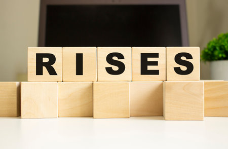 The word RISES is written on wooden cubes lying on the office table in front of a laptop. business concept.の写真素材