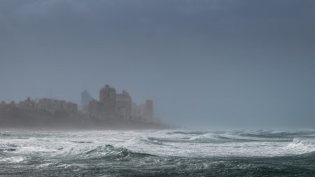 Stormy weather on seashore with big waves and silhouettes of buildings on high bank, Bat Yam, Israelの写真素材