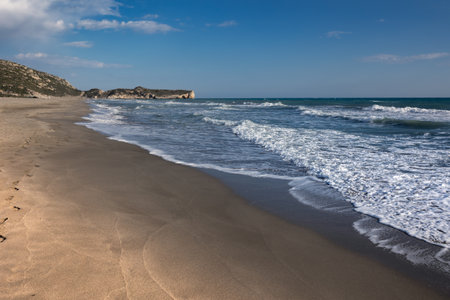 Long wide empty sandy beach with wavy sea and distant hills under clear blue sky, Patara, Turkeyの写真素材