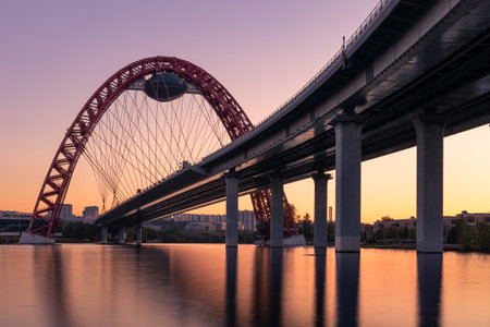 Sunset cityscape with modern arched cable stayed bridge reflecting in river water, Moscow, Russiaの写真素材