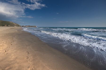 Long wide empty sandy beach with wavy sea and distant hills under clear blue sky, Patara, Turkeyの写真素材