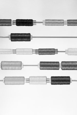 Many spools of thread of various sizes and colors arranged in rows on parallel thin rodsの写真素材