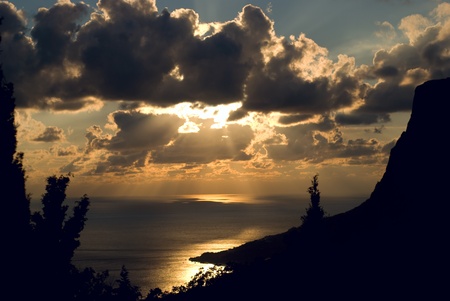 Sunset over large body of water with rays of light coming through cloudsの写真素材
