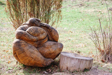 A figure of a pagan character made of wood sits on the ground next to a tree stumpの写真素材