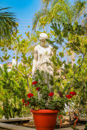 Stone statue of a woman stands in green bushes with flowers. High quality photoの写真素材