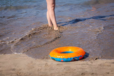 Female feet and small lifebuoy on the beach in the water