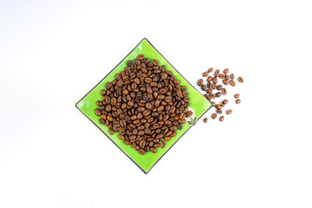 Coffee beans on a green square saucer, white backgroundの写真素材