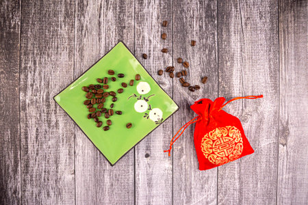 Coffee beans on a green saucer with a red bag next to it, wooden background, photo from aboveの写真素材