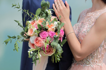 Beautiful bridal bouquet in hands of the bride. Wedding bouquet of peach roses by David Austin,  single-head pink rose aqua, eucalyptus, ruscus, gypsophilaの写真素材