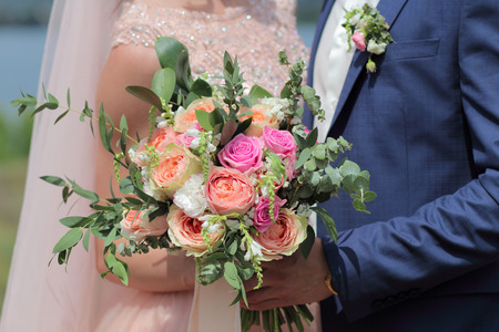 Bride holding a beautiful bridal bouquet. Wedding bouquet of peach roses by David Austin,  single-head pink rose aqua, eucalyptus, ruscus, gypsophilaの写真素材