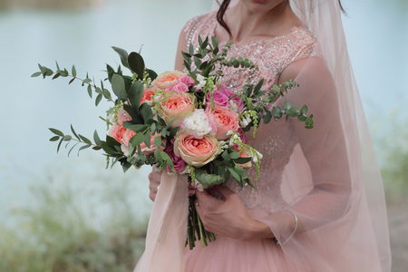 Bride holding a beautiful bridal bouquet. Wedding bouquet of peach roses by David Austin,  single-head pink rose aqua, eucalyptus, ruscus, gypsophilaの写真素材