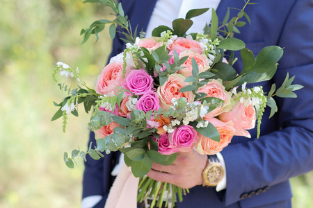 Beautiful bridal bouquet in hands of the groom. Wedding bouquet of peach roses by David Austin,  single-head pink rose aqua, eucalyptus, ruscus, gypsophilaの写真素材