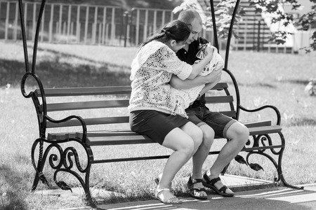 Young family sitting on a park bench. Father holding newborn daughter in her arms.Black and white photographyの写真素材