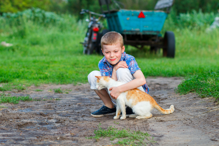 child plays with a red cat in the courtyard of a country houseの写真素材