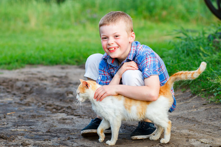 smiling little boy affectionately embraces a red cat. outdoorの写真素材