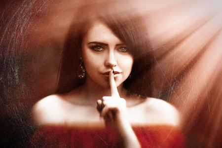 Young woman with dark long hair saying shh with forefinger on lips. silence gesture