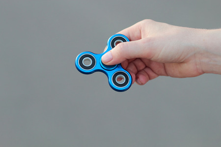 female hand holding popular fidget spinner toy on gray background, anxiety relief toy, anti stress and relaxation fidgetsの写真素材