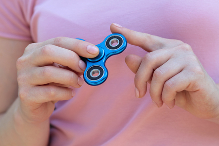 girl playing blue metal spinner in hands on the street, female hands holding popular fidget spinner toy on gray background, anxiety relief toy, anti stress and relaxation fidgetsの写真素材