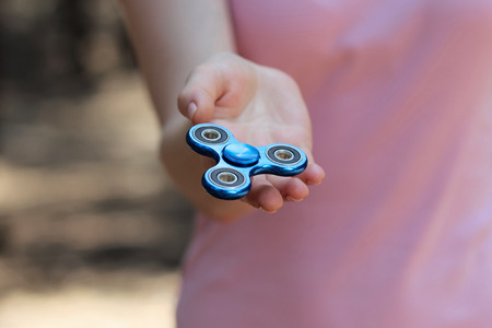 girl playing blue metal spinner in hands on the street, female hands holding popular fidget spinner...