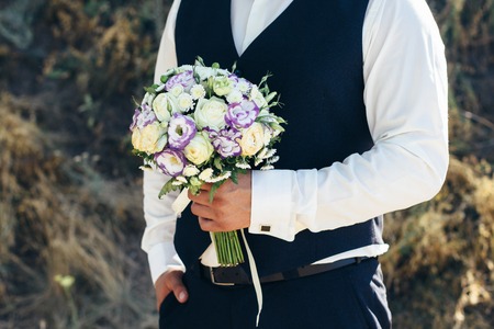 Wedding. The groom  in a white shirt  and waistcoat are holding bouquets of of white roses,...