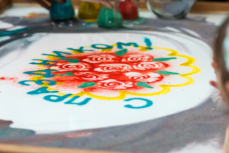 girl draws flowers and the word "Happy holiday" on the sand, sand animation, drawing sand closeupの写真素材