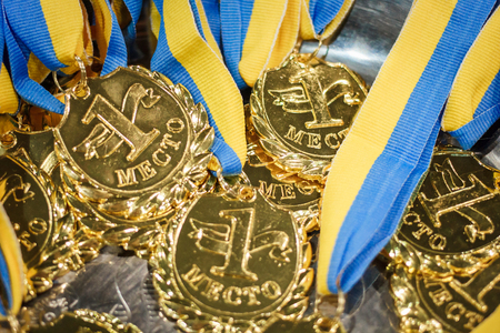 A lot of gold medals with yellow ribbons on a silver tray, awards of champions, sport achievements, first place, prize for the winner, it is written on a medal - first placeの写真素材