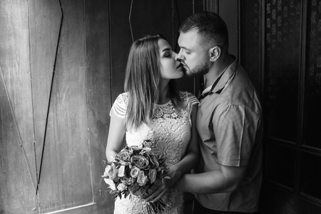 portrait of a romantic couple,man and woman kissing in a dramatic light, girl holding flowers in hands, young beautiful bride in white dress holding wedding bouquet, black and white photography .の写真素材