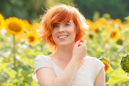 young girl enjoying nature on the field of sunflowers at sunset, portrait of the beautiful redheaded...