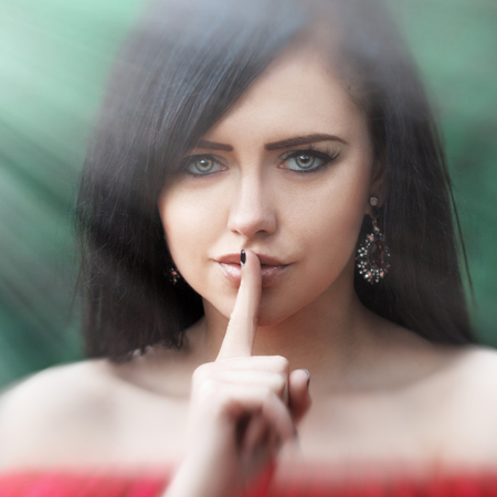 Young woman with dark long hair saying shh with forefinger on lips. silence gestureの写真素材