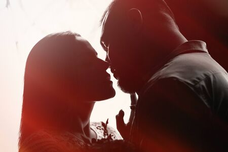 portrait of a romantic couple in a backlight from a window or door, silhouette of a couple in a doorway with a backlight, couple of lovers groom and bride at the window, girl holding flowers in handsの写真素材