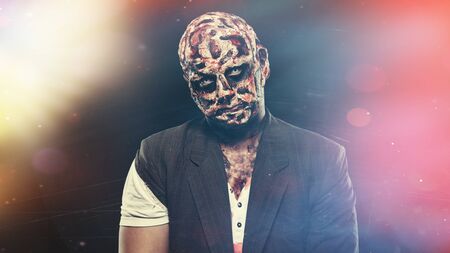 scary halloween theme and halloween makeup: scary man with a burnt face holds a baseball bat in his hands, serial maniac in a ragged suit, evil or angry superhero on a black backgroundの写真素材