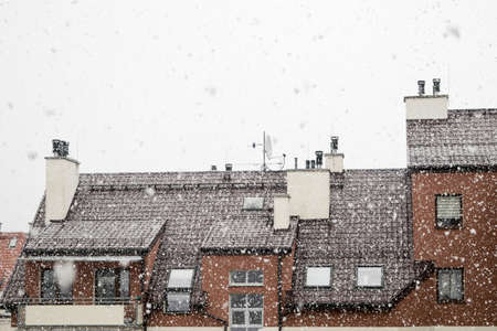 Snow white, large flakes of falling snow, view of the roof of the building with mounted antennas and ventilation pipes against the gray skyの写真素材